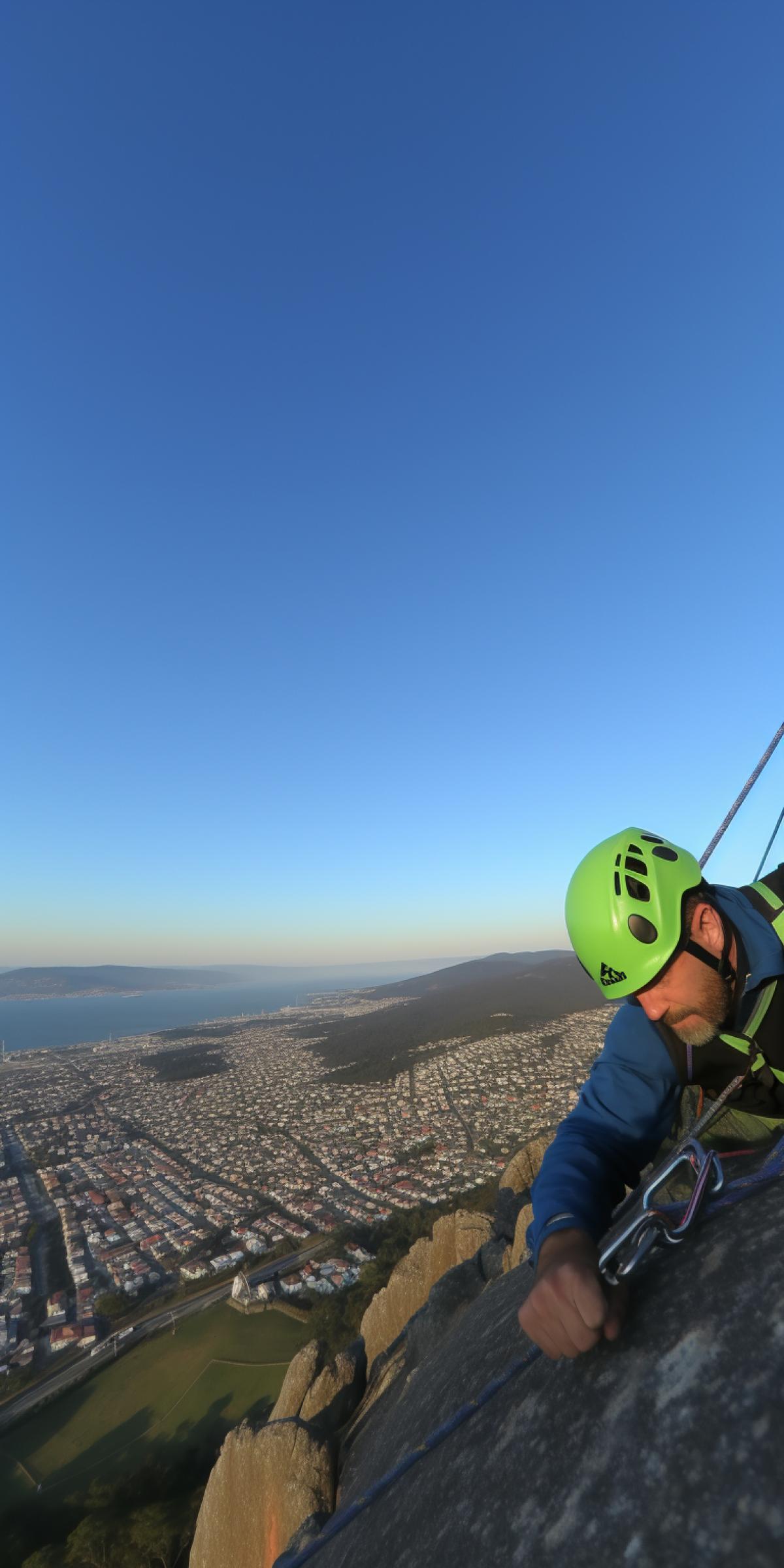 a climber wearing full mountaineer equipment is ascending a skyscraper in a futuristic city, dawn, sunrays reflect in windows