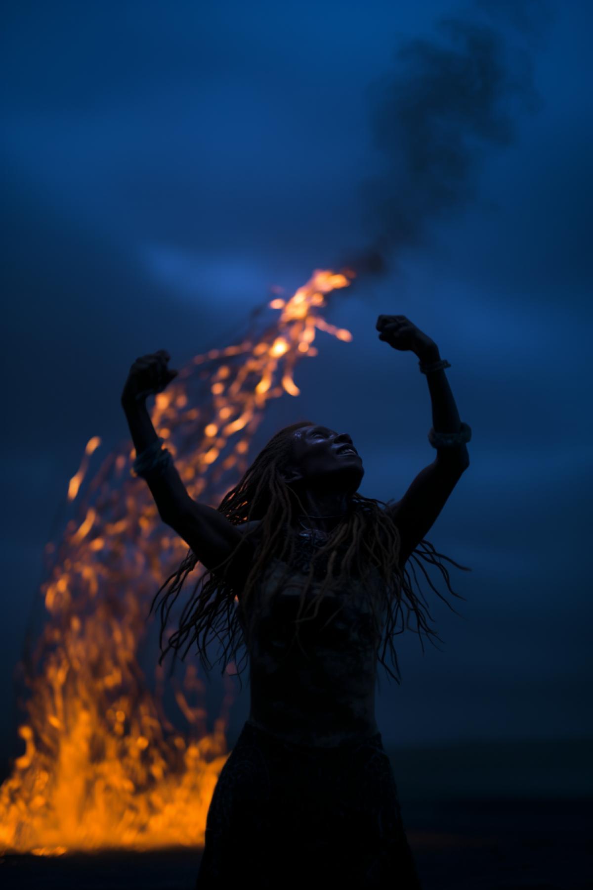 a young female shaman of an African tribe dances the dance of calling rain, in full body, near a fire in the desert