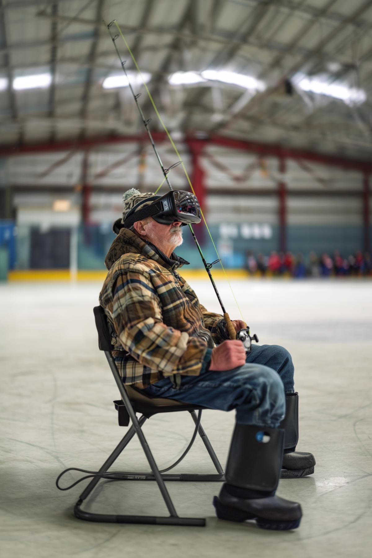 A fisherman with a fishing rod sits in the middle of a hockey field wearing virtual reality glasses.