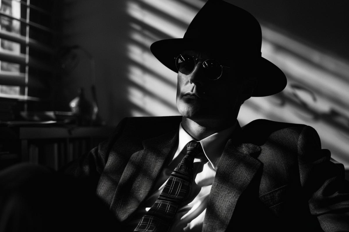 Detective sits in his office, shadows hide his eyes under his hat, noir
