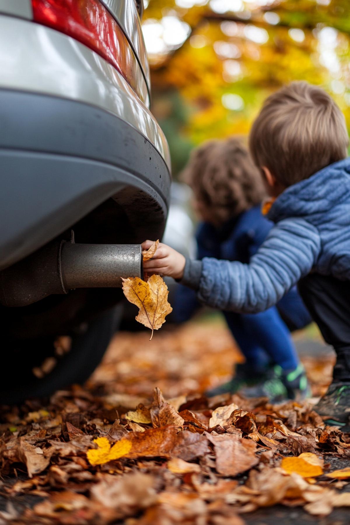 Children push fallen autumn leaves into a car exhaust pipe