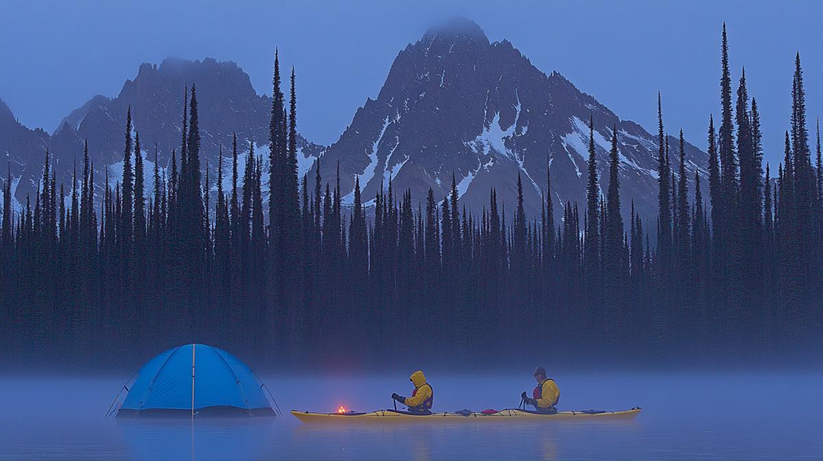 Scene of an exciting adventure on the water, dawn, calm surface of the lake, bright sun rays breaking through tall trees, dense forest around, two kayakers in bright life jackets rowing slowly, low mountains can be seen in the distance, the reflection of mountains and forests in the mirror surface of the water, a tent on the shore with a lit fire and neatly folded equipment, morning fog spreading across the water, light ripples around the kayaks, clear blue sky with rare clouds, an atmosphere of calm tranquility, realistic details, soft shadows and warm light, the weather is warm, ideal for an early morning in nature .