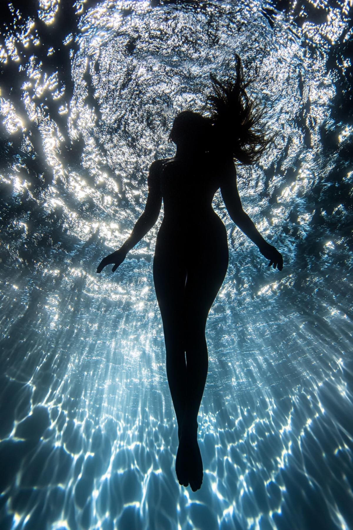 Looking up from the bottom of the sea at the girl floating above. Looking up from under the water.