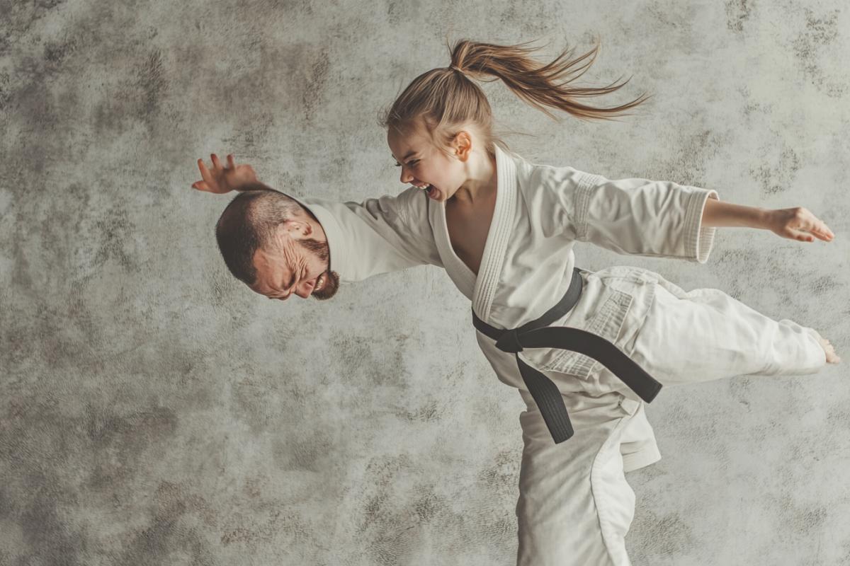 A little funny girl Karatist in a white kimono with a dark belt throws a man through the head
