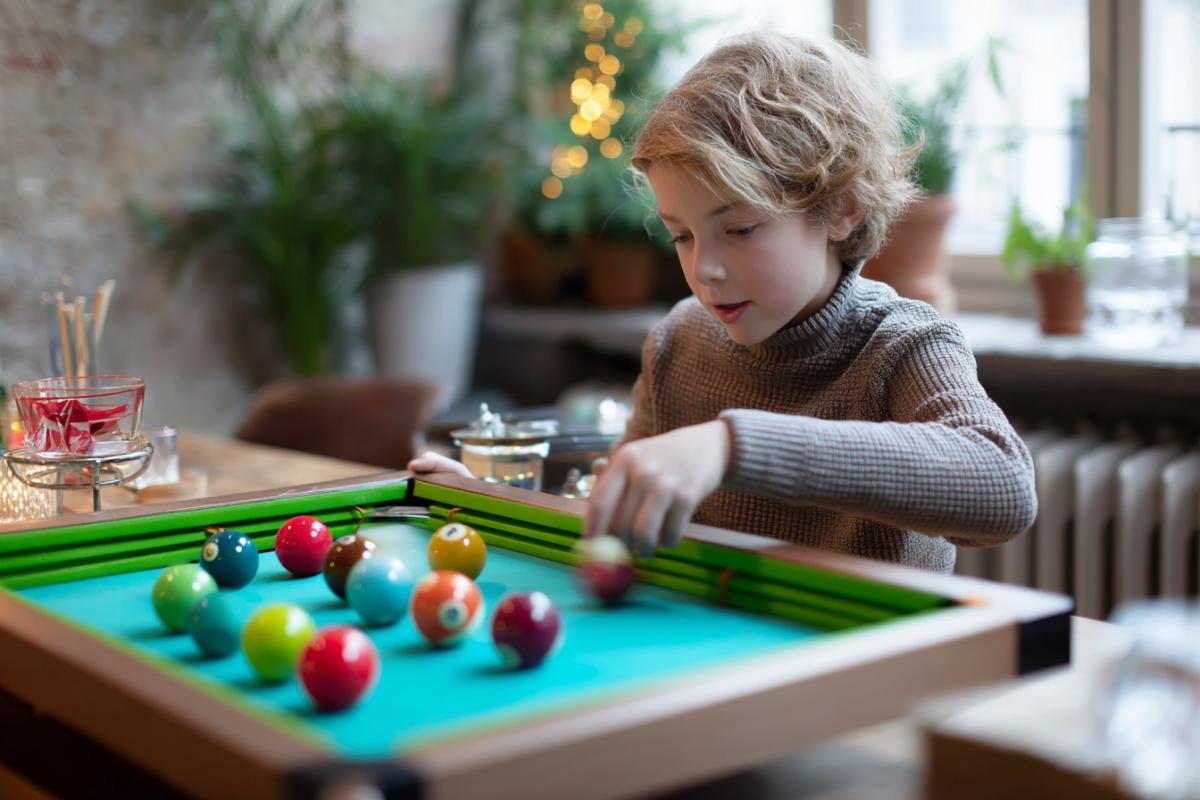Children play small desktop billiards that simulates the present, but in a reduced size