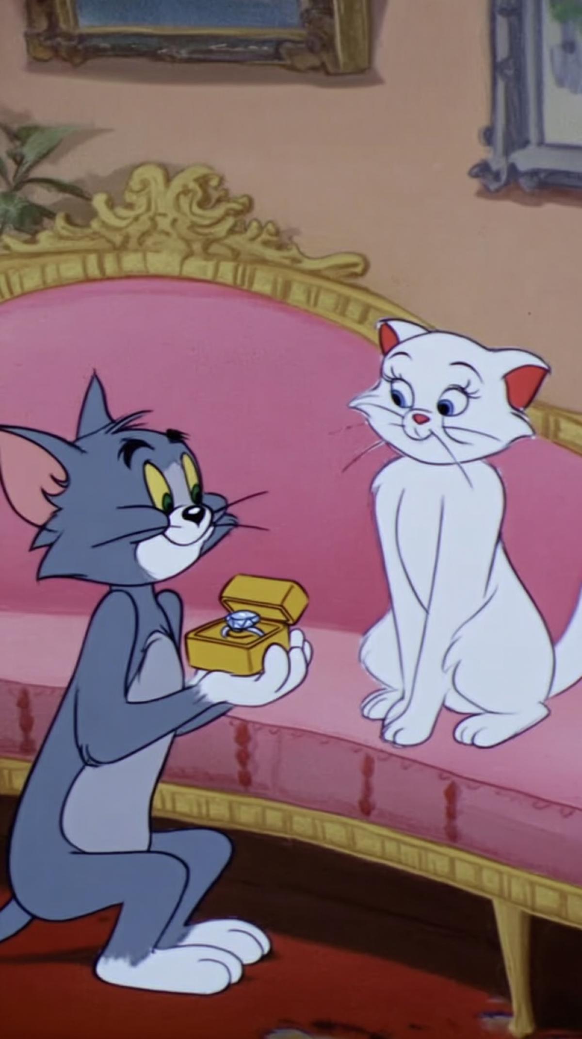 a shot from the Tom and Jerry cartoon, Tom the cat gives a diamond ring to a white cat who is sitting on the couch, a marriage proposal