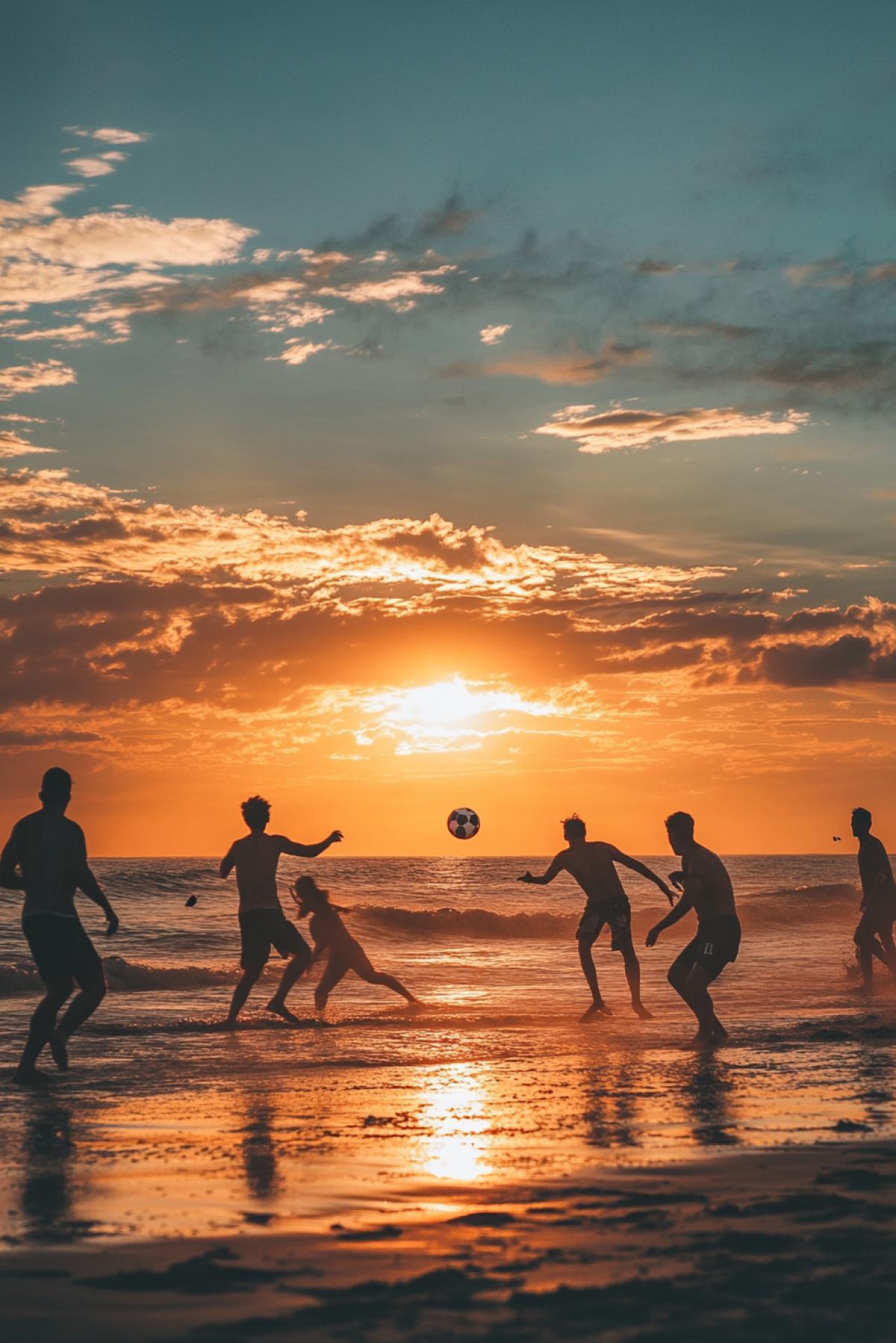People play beach football on the background of sunset