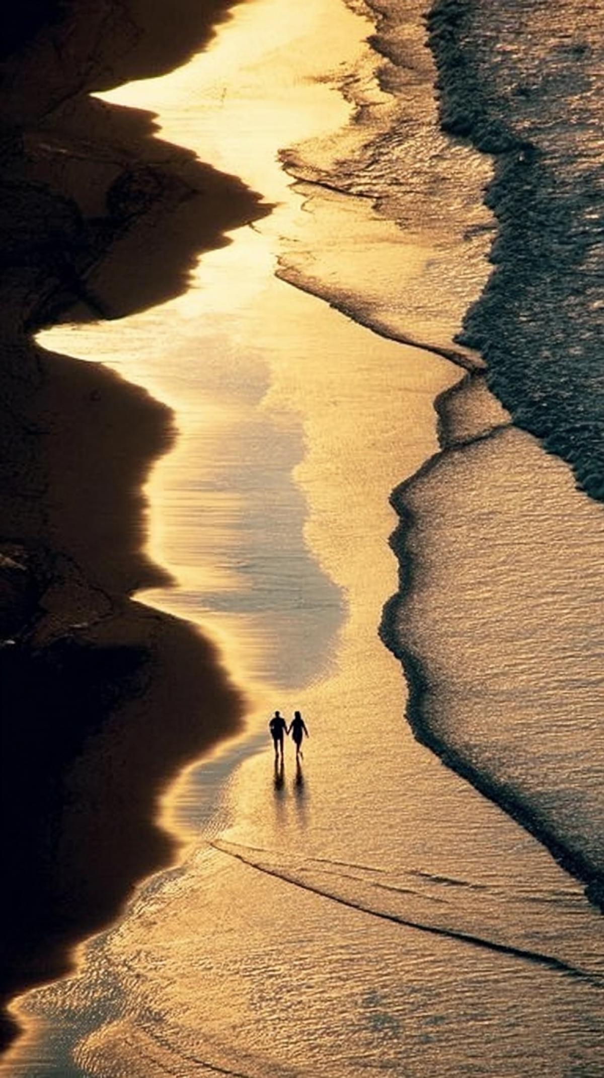 A birds-eye view of lovers holding hands, walking along the ocean shore