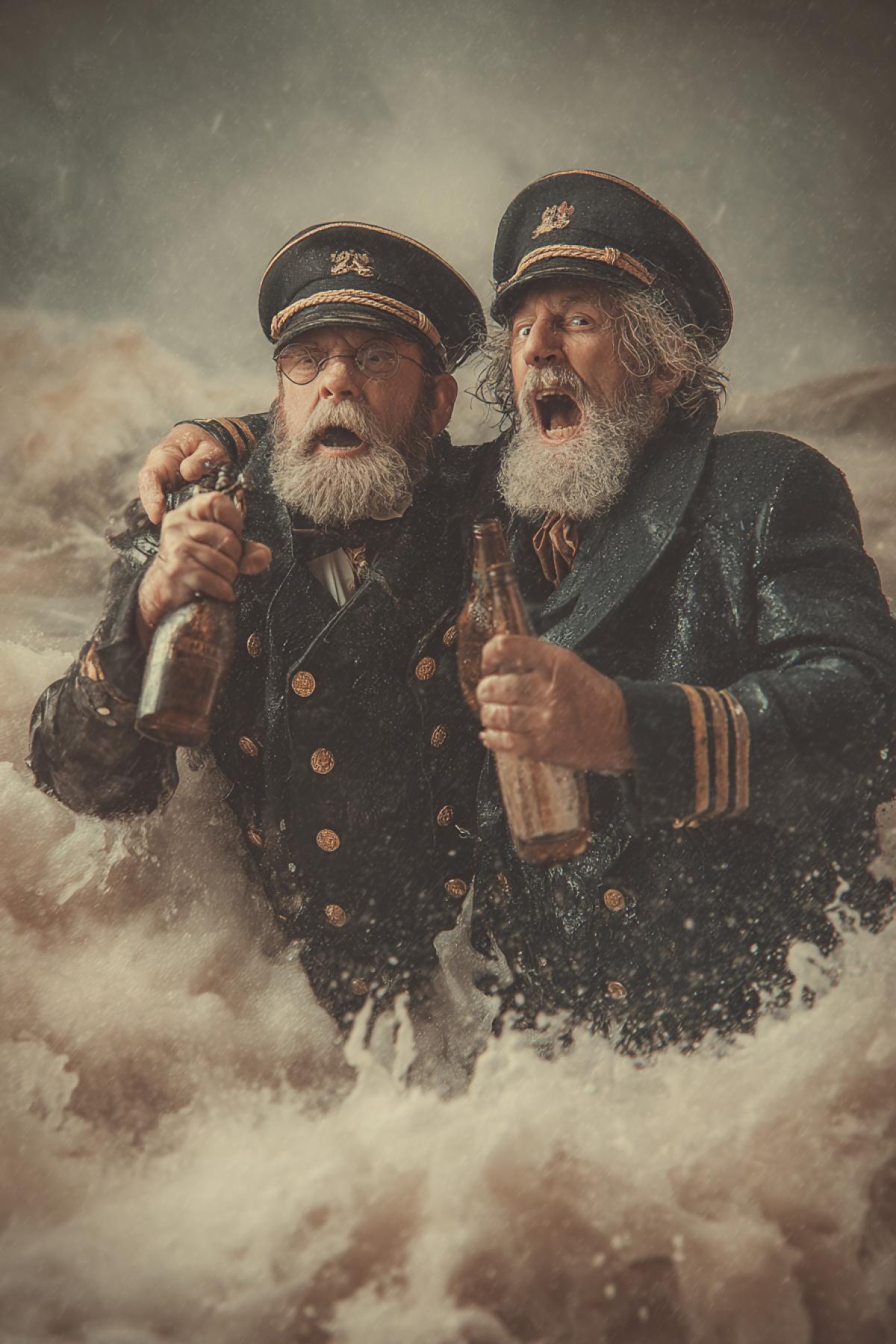 Two old sailor captains drowning sinking in deep storming sea on the background of their destroyed vessels clinking cheers with their flasks hopelessness