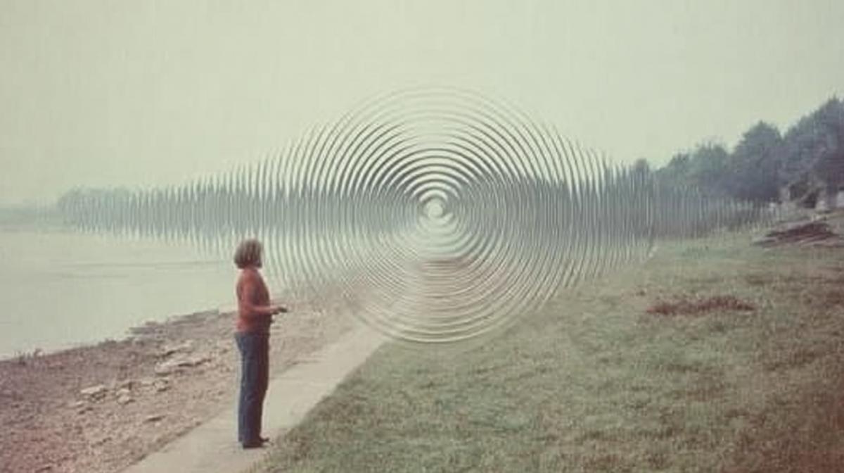 A photograph of an optical illusion in the form of sound waves hung in the air, with a woman standing next to him. Aesthetics of the photo of the 1970s, there is a little fog around, as if this is a transition to another world, a matrix