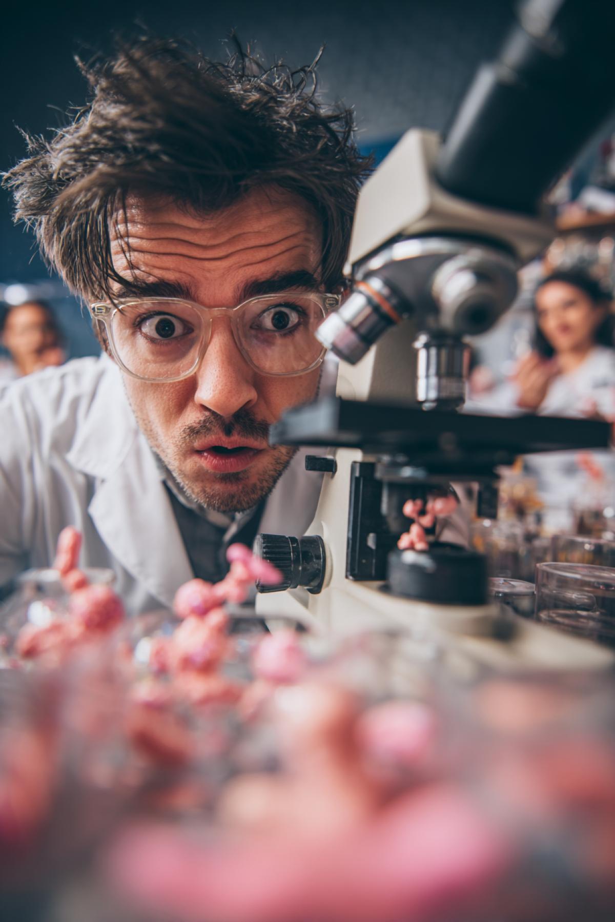 Young handsome scientists in laboratory absolutely scared with the view in his microscope he sees amoebae microscopic girls dancing ironic photo high quality lots of details