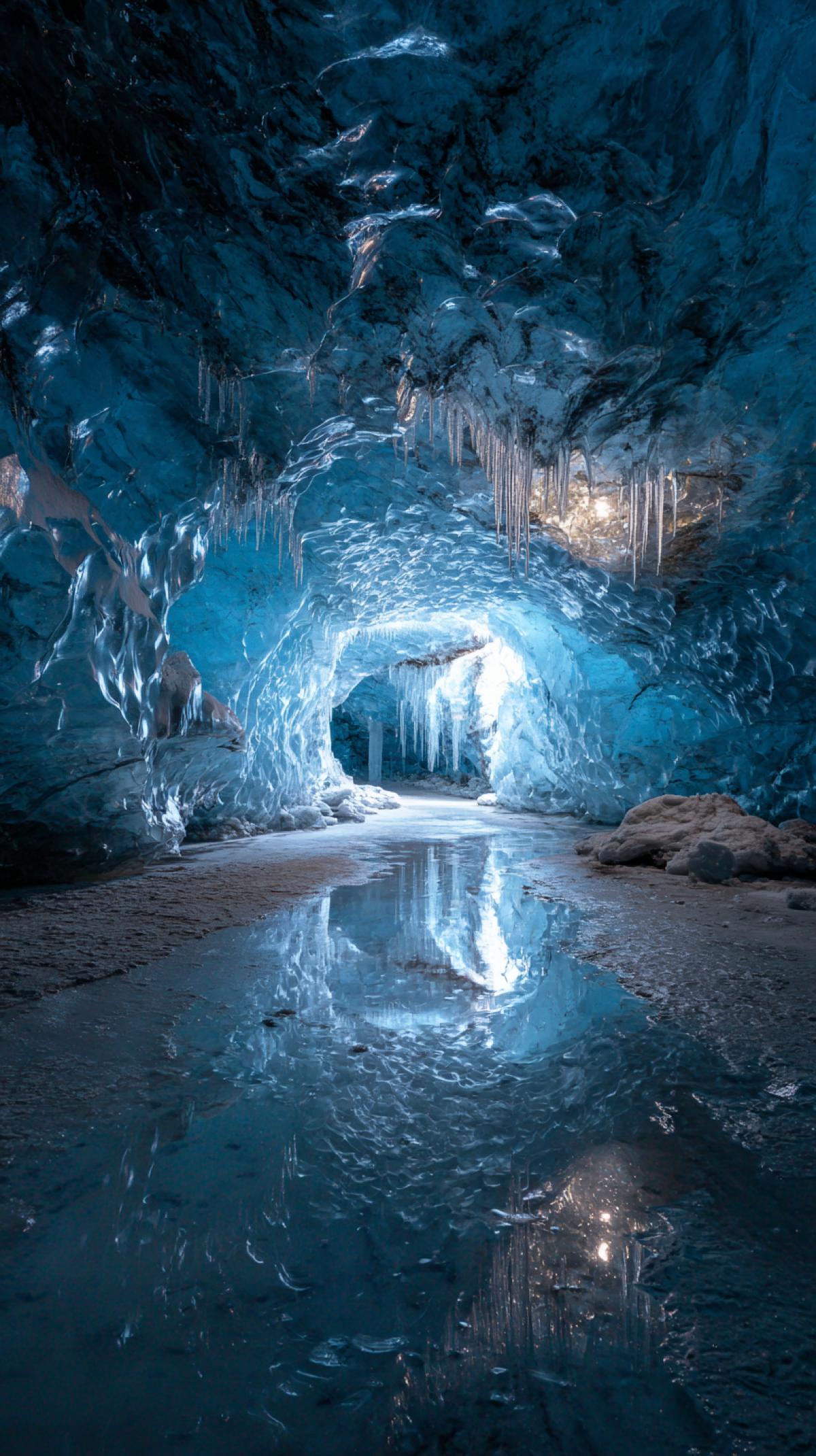 The interior of the ice cave. The scale, ice texture and the game of light are rays, walls, crystalline formations, frozen stalactites/stalagmites, reflection in reservoirs inside the cave, traces of humans and animals. Neon light