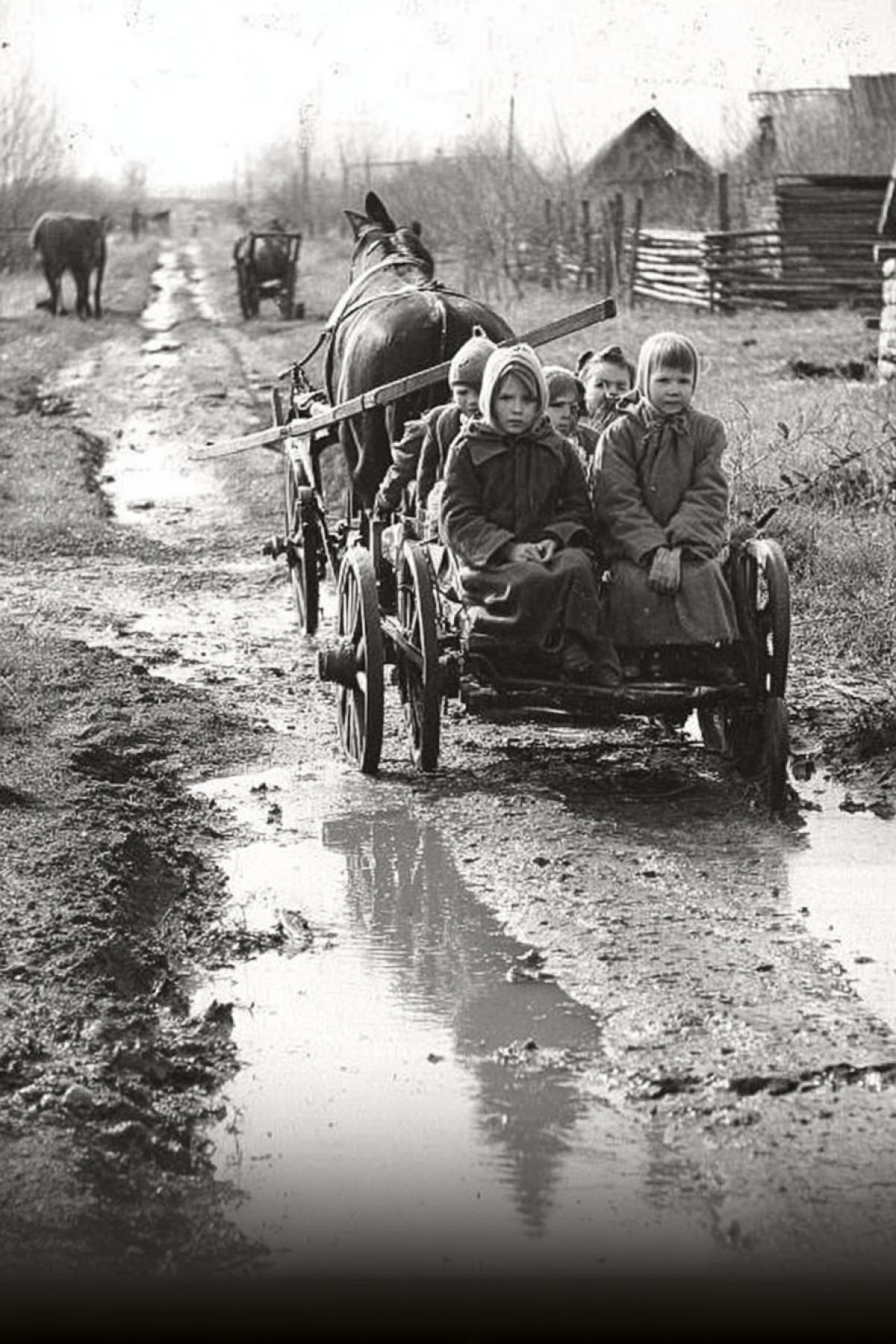 8-year-old schoolchildren riding a cart, horse-drawn carriage, horse with its back in the frame, dirt road, puddles and mud, deep autumn, children wearing fur coats and hats, schoolbag, Russian village, 1960, dark-and-white photo