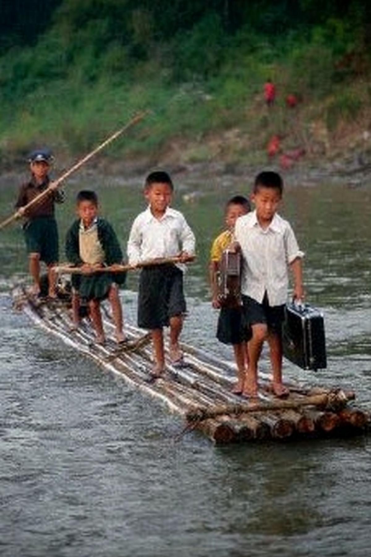 schoolchildren on a homemade bamboo raft crossing a river, 8-year-old boys with briefcases, China, photo