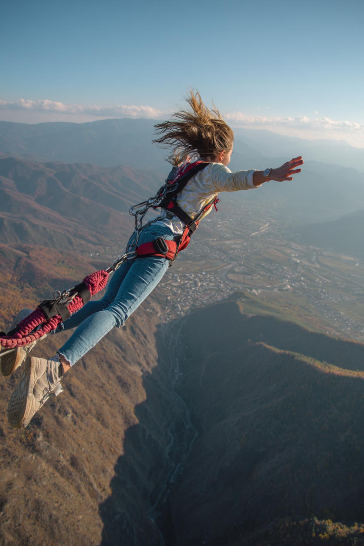 Bungee jumper 23yo beautiful girl at the moment a second before landdiving flying she is scared fear in eyes detailed breathtaking photo on the background of valley far below