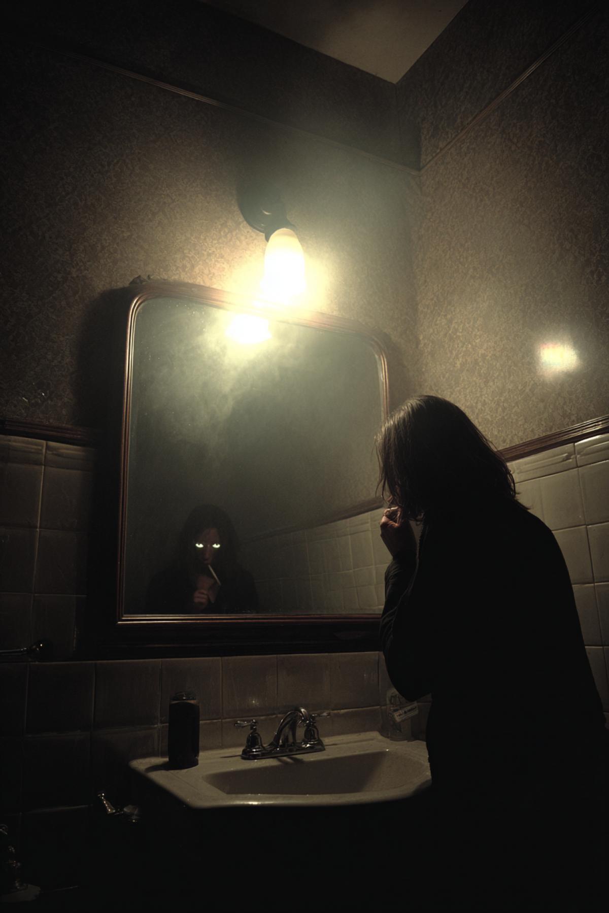 A dimly lit, vintage bathroom at night. A person is brushing their teeth at the sink, unaware that in the foggy mirror reflection, a tall, shadowy figure with glowing white eyes is standing directly behind them. The only light comes from a single faulty bulb, casting dramatic shadows. Horror movie still, anamorphic lens flare, high contrast, masterful lighting, terrifying implication.