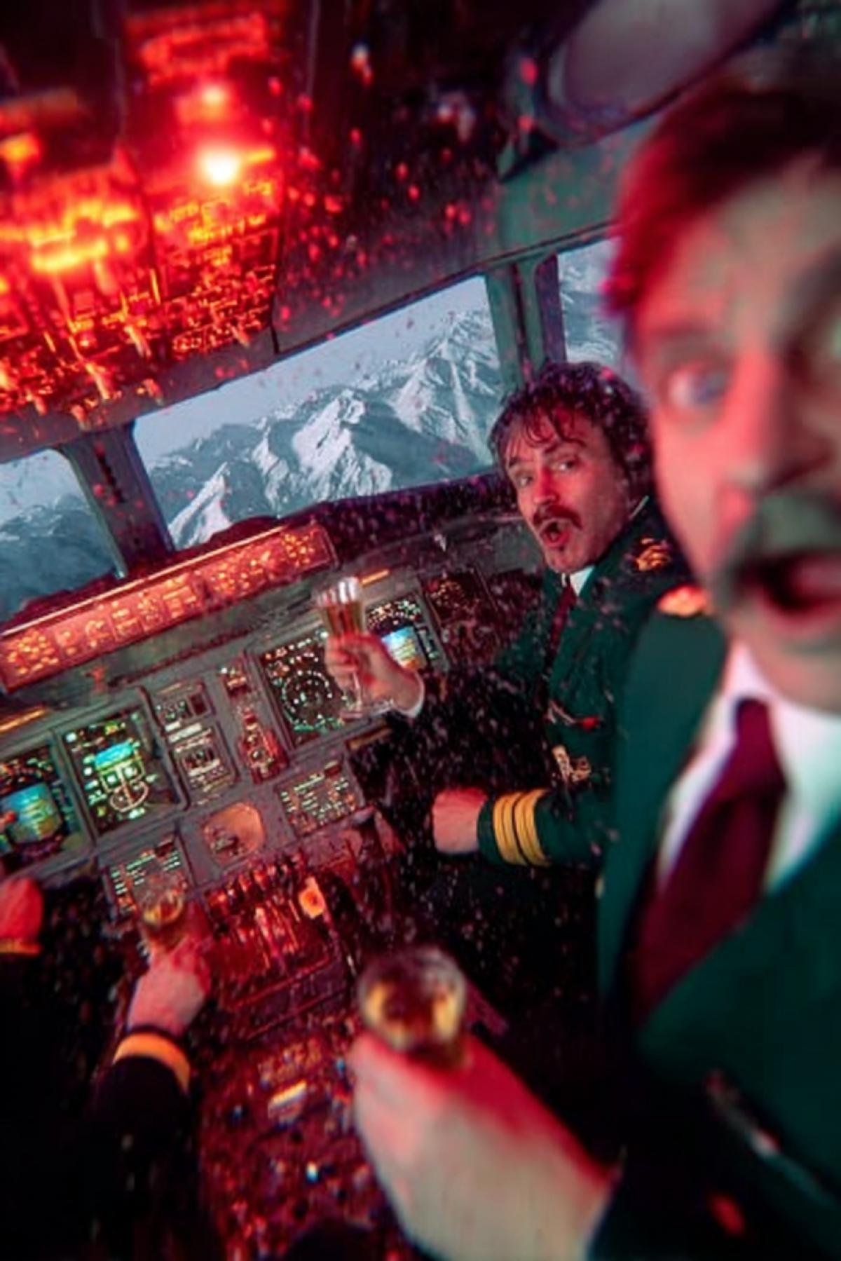 Wide-angle lens shot of an aircraft cockpit. Bright red warning and danger lights are flashing. Through the windshield, approaching mountains are visible catastrophe is inevitable. The pilots are opening sparkling champagne and pouring it into glasses. Champagne foam spills onto control panels, bubbling around switches and indicators. The flight attendants joyful dance creates blurred motion in the tense scene. Mountain peaks terrifyingly close to the windshield, details of rocks visible. Pilots faces show strange euphoria mixed with fatalistic acceptance. Emergency sirens flash red light on champagne glasses and smiling faces. Everyone is celebrating as if for the last time. Hyperrealistic, 8k, surreal atmosphere.