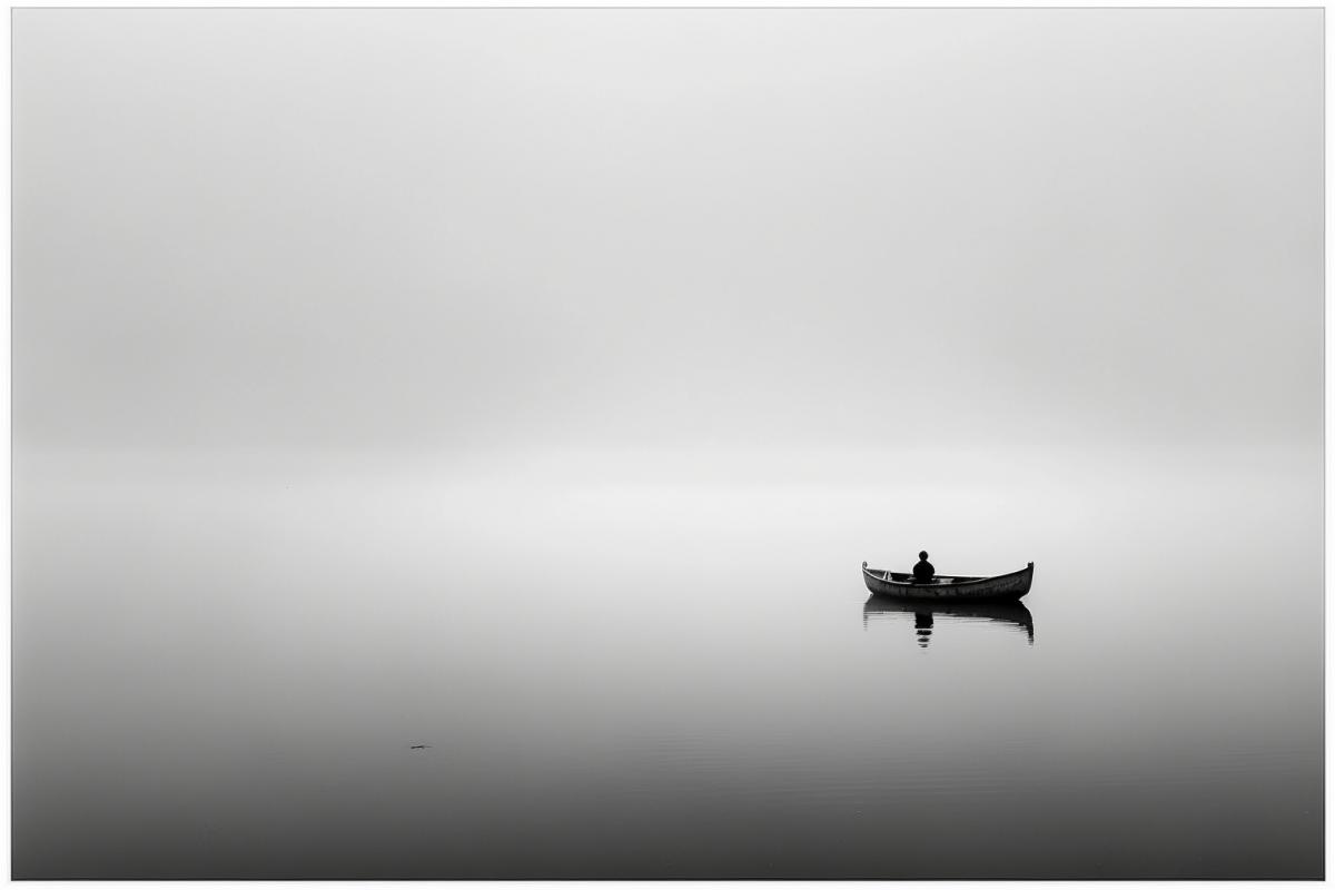 A serene lake shrouded in mist, with a solitary boat drifting towards a distant horizon, symbolizing the journey to the afterlife. (Keywords) Reflection, transition, solitude, serenity, transcendence. (Camera type) Digital SLR camera. (Lens type) Standard prime lens. (Time of day) Dawn. (Photograph style) Minimalistic.